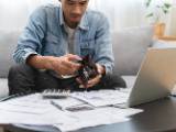 Un homme devant son ordinateur regarde son portefeuille vide.