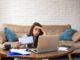 Une femme devant son ordinateur regarde des documents en soupirant. 